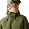 Person mit lockigem blondem Haar, beige Strickmütze und Skibrille auf dem Kopf, trägt olivegrüne Kapuzenjacke, Blick nach rechts