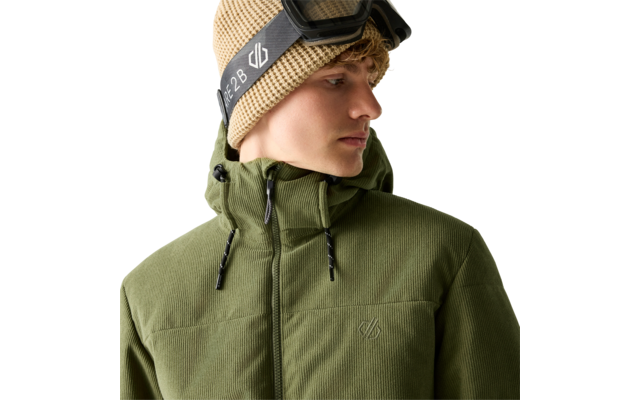 Person mit lockigem blondem Haar, beige Strickmütze und Skibrille auf dem Kopf, trägt olivegrüne Kapuzenjacke, Blick nach rechts