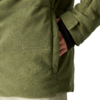 Nahaufnahme einer grünen Cordjacke mit seitlicher Tasche, teilweise hineingesteckter Hand, sichtbarem schwarzen Ärmel und hellem Hintergrund