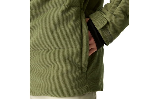 Nahaufnahme einer grünen Cordjacke mit seitlicher Tasche, teilweise hineingesteckter Hand, sichtbarem schwarzen Ärmel und hellem Hintergrund