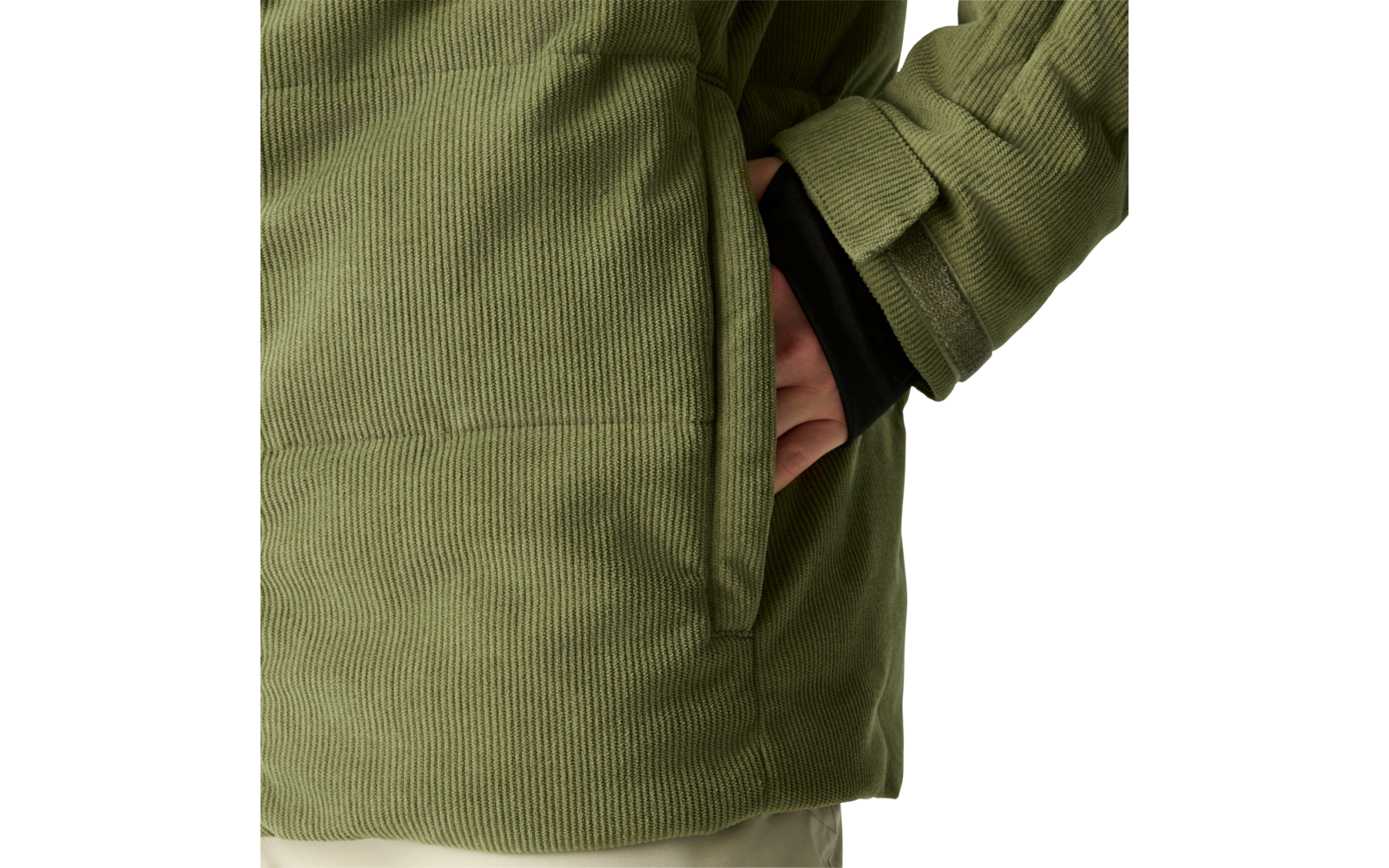 Nahaufnahme einer grünen Cordjacke mit seitlicher Tasche, teilweise hineingesteckter Hand, sichtbarem schwarzen Ärmel und hellem Hintergrund