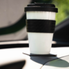 White reusable travel cup with black lid and black silicone band on a car dashboard