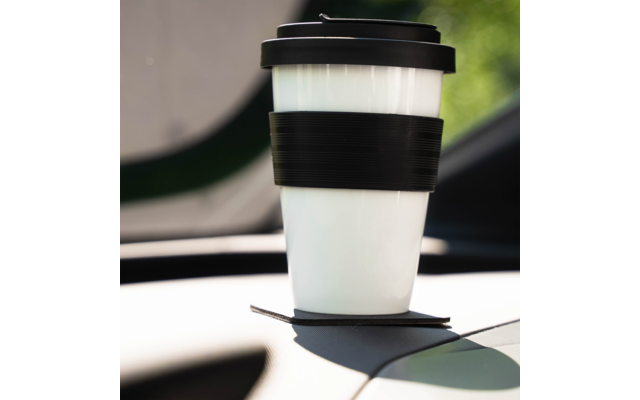 White reusable travel cup with black lid and black silicone band on a car dashboard