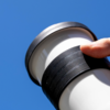 Hand holding a white tumbler with a black ribbed grip against a blue sky