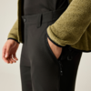 Plano detalle: mano derecha en el bolsillo lateral con cremallera de unos pantalones negros; chaqueta de punto verde y top negro visibles