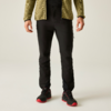 Parte inferior del cuerpo de una persona de pie con chaqueta de forro polar verde oliva, pantalones negros y zapatos negros con suelas rojas sobre fondo claro