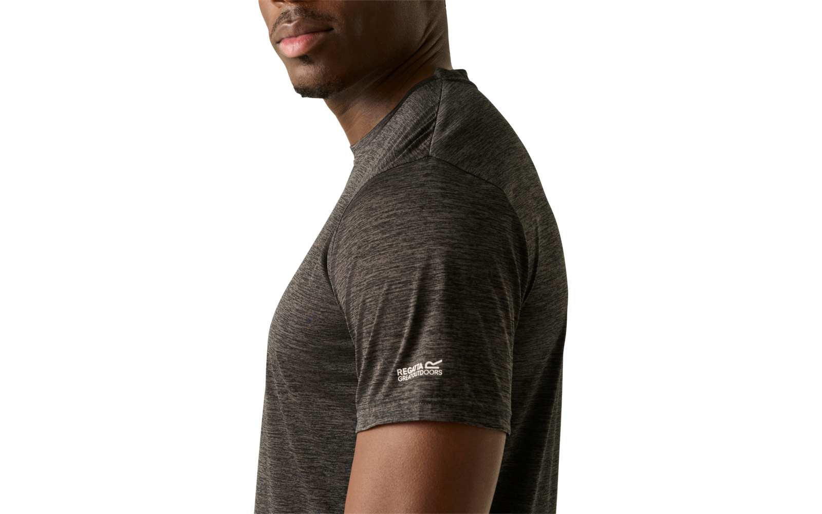 Seitenansicht eines Mannes mit dunkler Haut, der über die Schulter zur Kamera blickt, trägt ein dunkelgraues kurzärmeliges T‑Shirt vor hellem einfarbigem Hintergrund