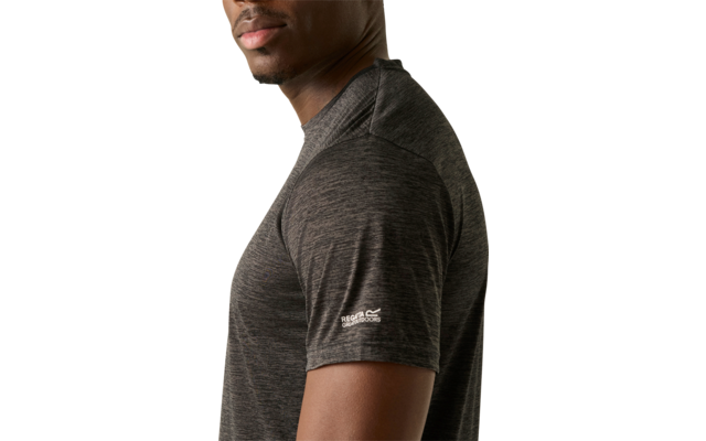 Seitenansicht eines Mannes mit dunkler Haut, der über die Schulter zur Kamera blickt, trägt ein dunkelgraues kurzärmeliges T‑Shirt vor hellem einfarbigem Hintergrund