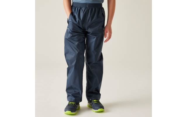 Onderlichaam van een persoon in donkerblauwe regenbroek en blauwgroene sportschoenen