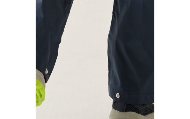 Donkerblauwe broekspijpen, links een neongele handschoen, rechts een donkergrijze sneaker met licht beige zool op een lichte achtergrond