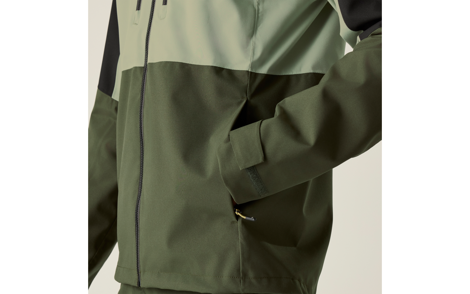 Zweifarbige grüne Jacke mit Reißverschluss, sichtbarer Seitentasche und Hand in der Tasche