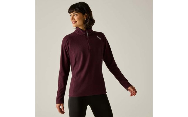 Personne devant un fond gris clair portant un pull bordeaux à manches longues avec une fermeture éclair courte et un petit logo sur la poitrine gauche, legging noir, regard vers la gauche