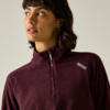 Personne aux cheveux foncés mi-longs et boucle d'oreille créole, regard vers la gauche ; porte un pull polaire bordeaux avec une petite fermeture éclair et un petit logo blanc, fond clair
