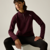 Personne assise sur un cube blanc, porte un pull bordeaux à demi-fermeture éclair, legging noir, cheveux courts foncés, clous d'oreille, arrière-plan clair neutre
