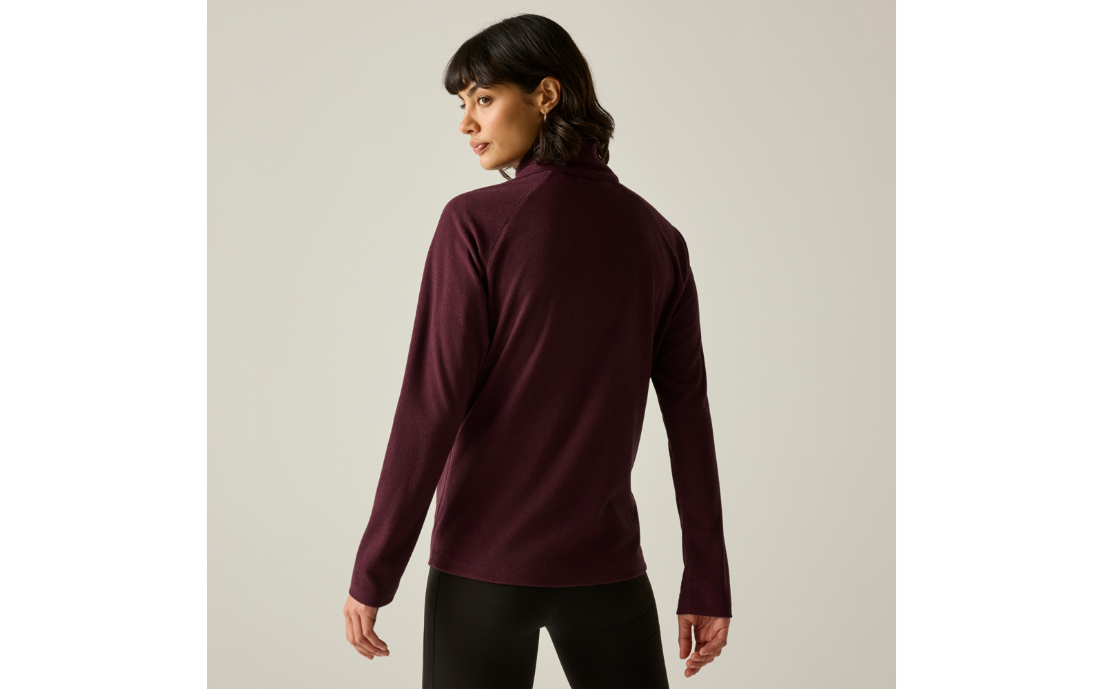Personne vue de dos, portant un pull à col roulé bordeaux et un pantalon noir sur fond uni clair