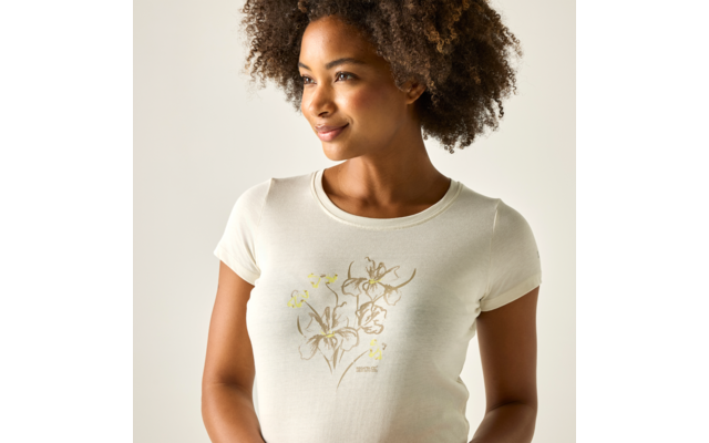 Femme aux cheveux bouclés, demi‑portrait ; elle porte un t‑shirt clair à motif floral, regarde sur le côté et sourit légèrement sur fond clair
