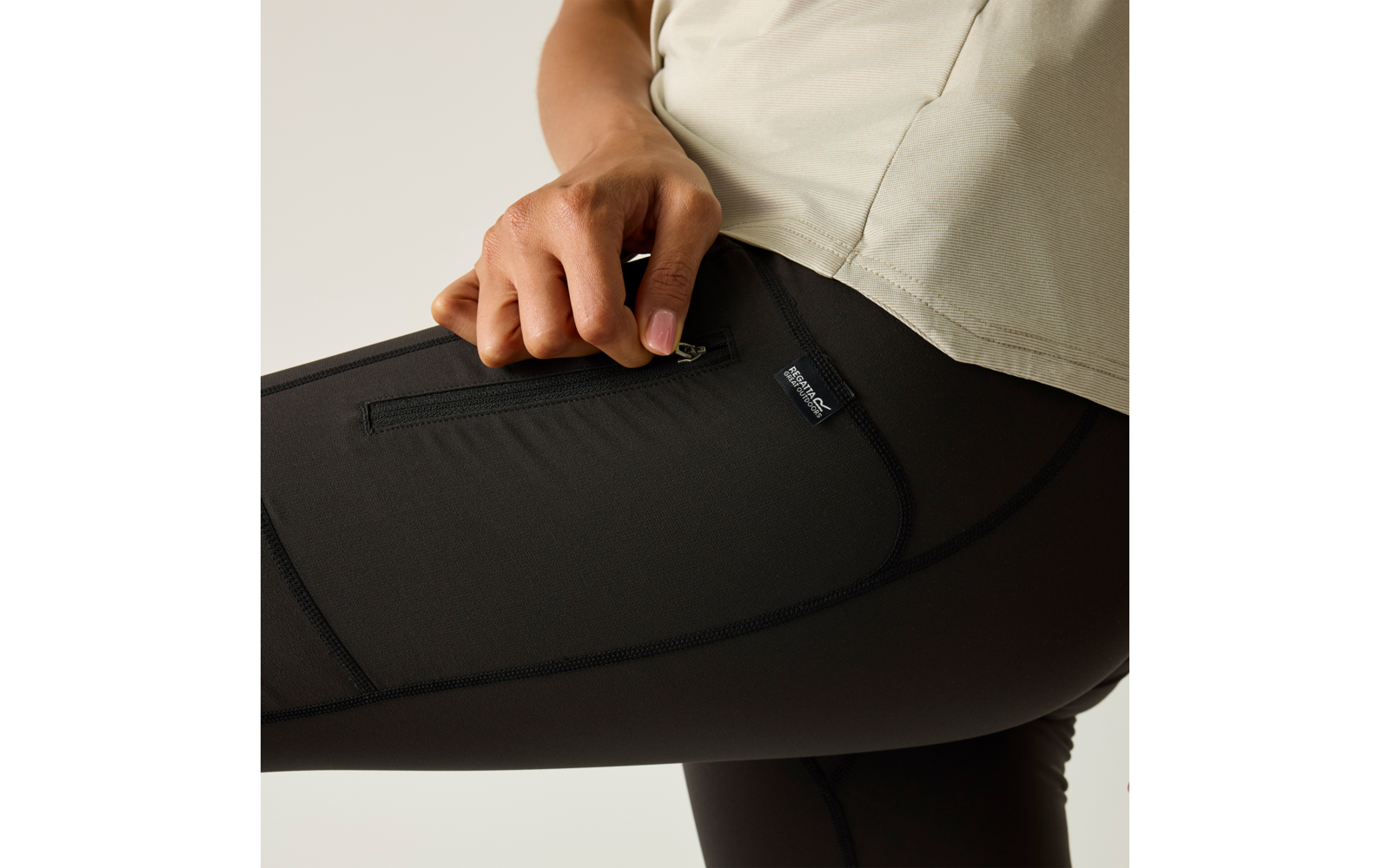 Nahaufnahme einer Hand, die an der Reißverschlusstasche an schwarzen Leggings zieht; heller Oberteilansatz sichtbar