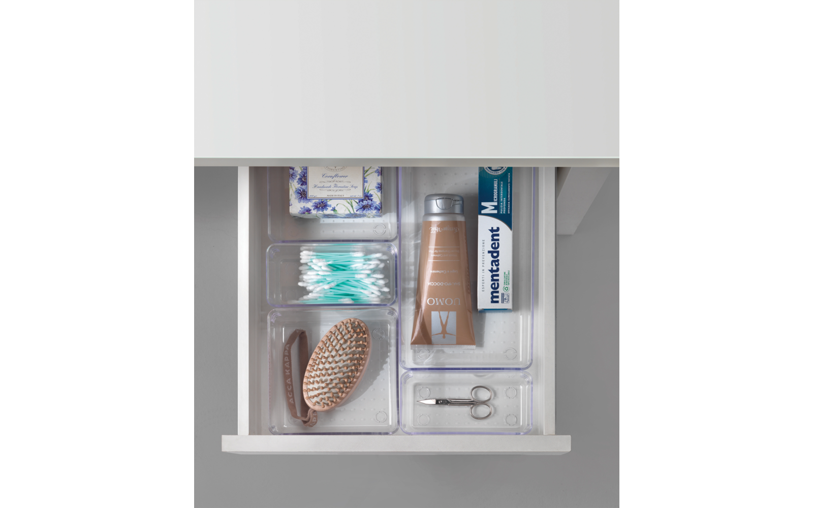 Tiroir ouvert avec une brosse marron, des cotons-tiges, une brosse à dents, un paquet de mouchoirs et du dentifrice