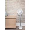 Ventilateur sur pied à droite, meuble en bois à gauche avec deux vases en céramique, mur avec lattes de bois horizontales, plinthe blanche