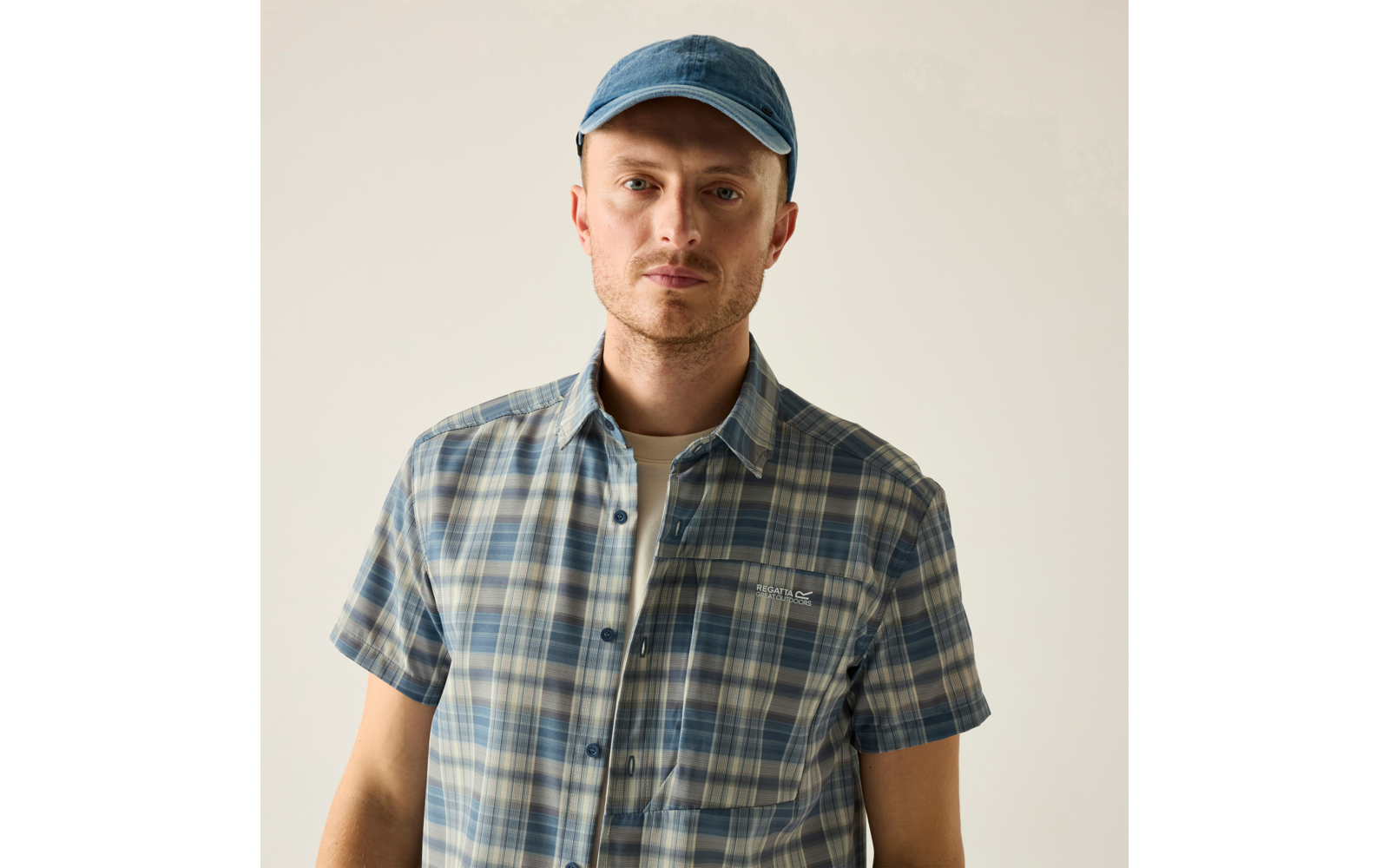 Mann mit blauer Baseballkappe und blau kariertem Kurzarmhemd vor hellem Hintergrund, schaut in die Kamera