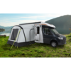 Camper van with attached tent on a green meadow near a lake and mountains in the background