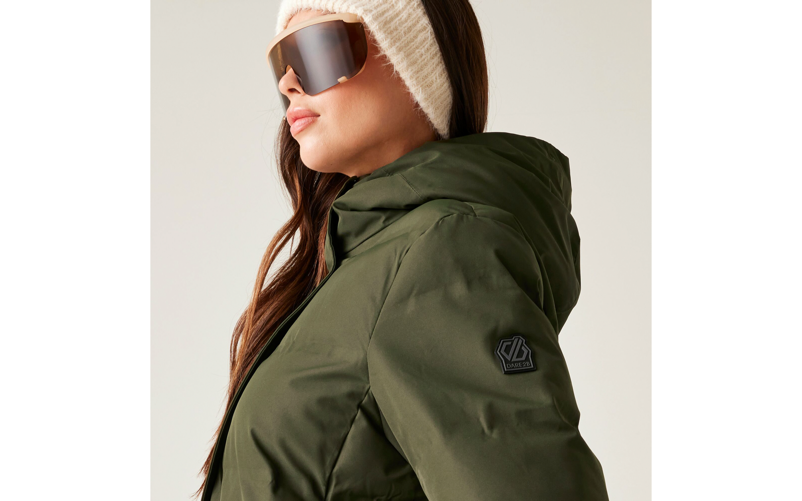 Frau mit Sonnenbrille, beiger Mütze und grünem Wintermantel mit Kapuze