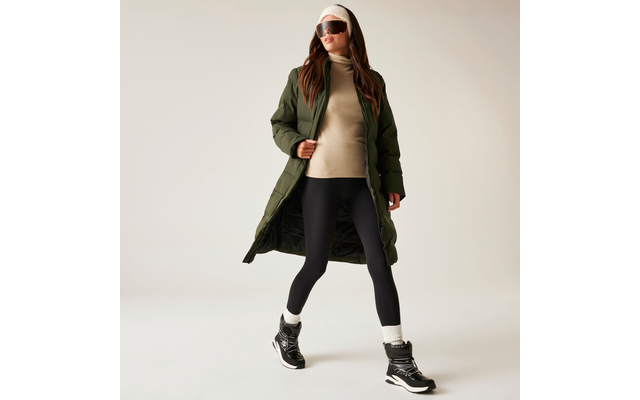 Frau mit Sonnenbrille, langer grüner Jacke, beigem Pullover, schwarzer Leggings und schwarzen Stiefeln beim Gehen