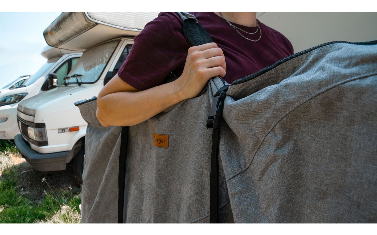 Person carrying two gray bags in front of a white camper van