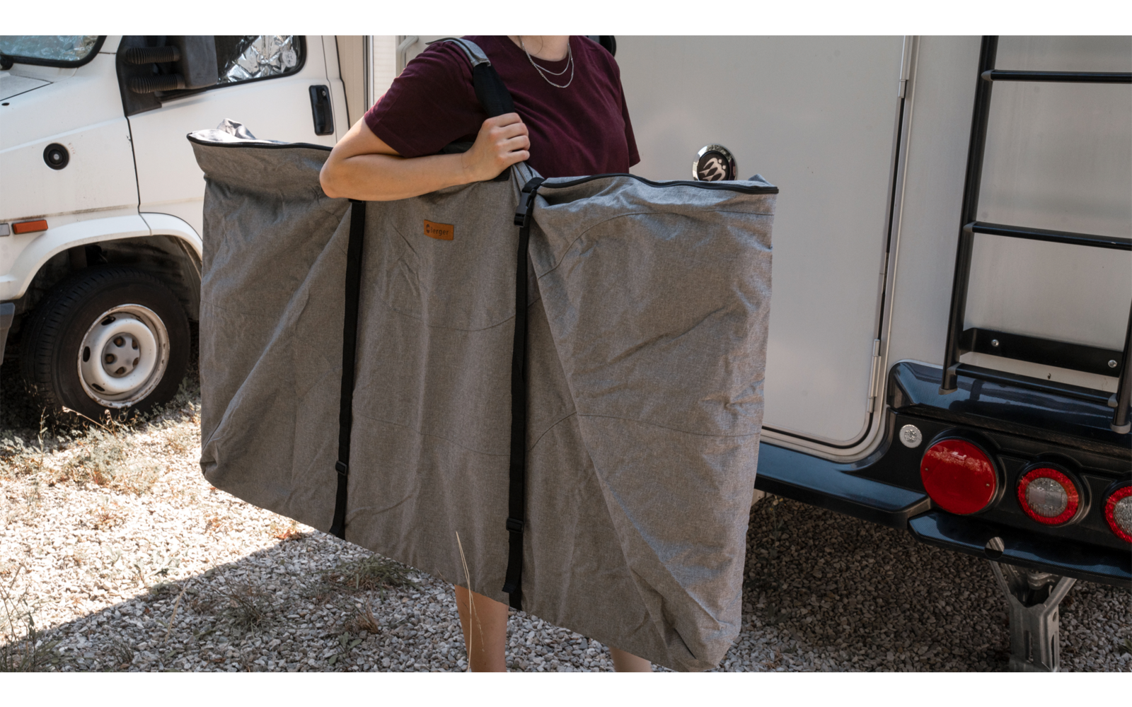 Person carrying two large gray bags in front of a white camper van