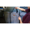 A person is holding a large gray carrying bag with black handles and straps