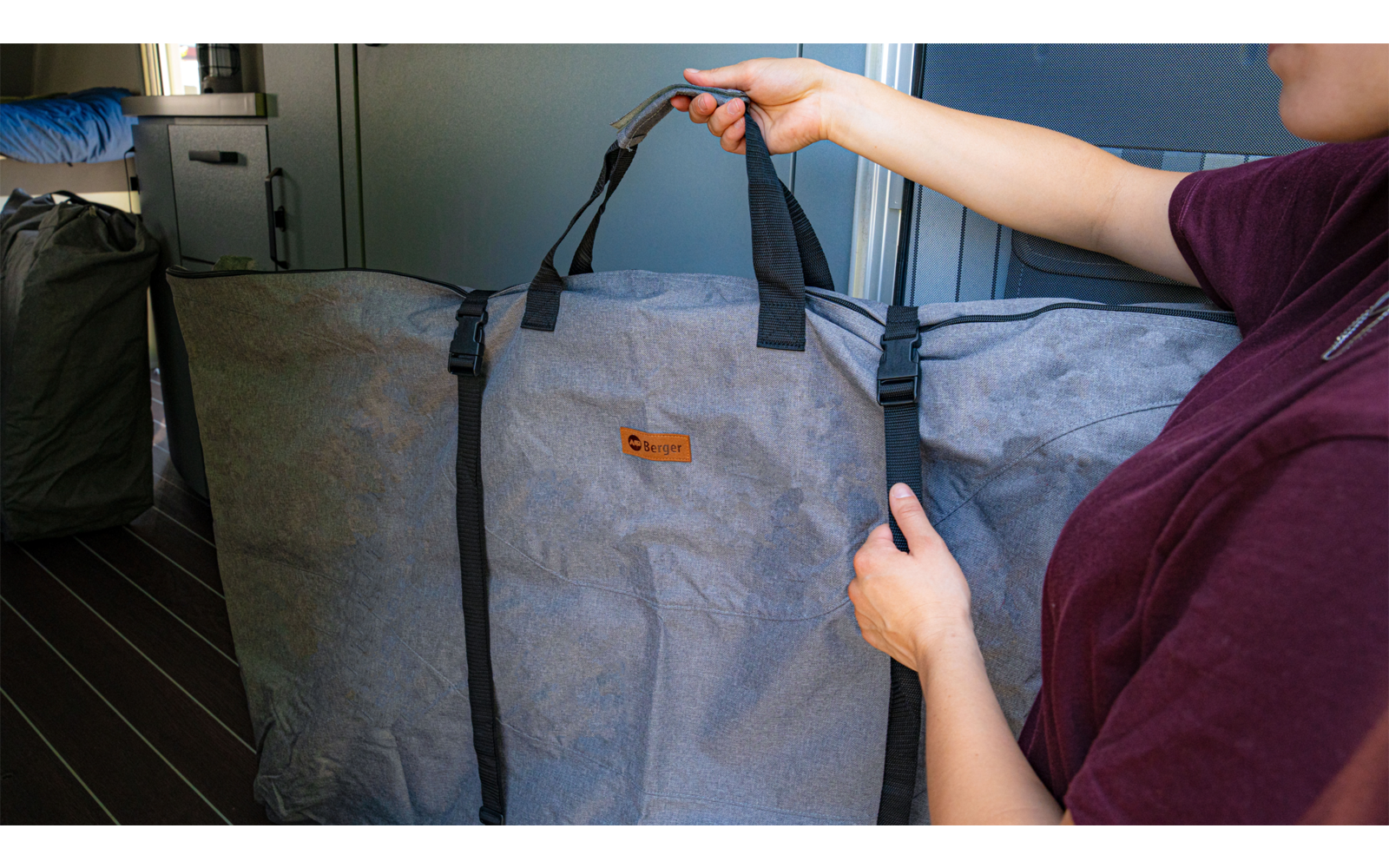 A person is holding a large gray carrying bag with black handles and straps