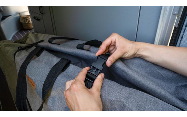 Hands fastening a black buckle on a gray bag