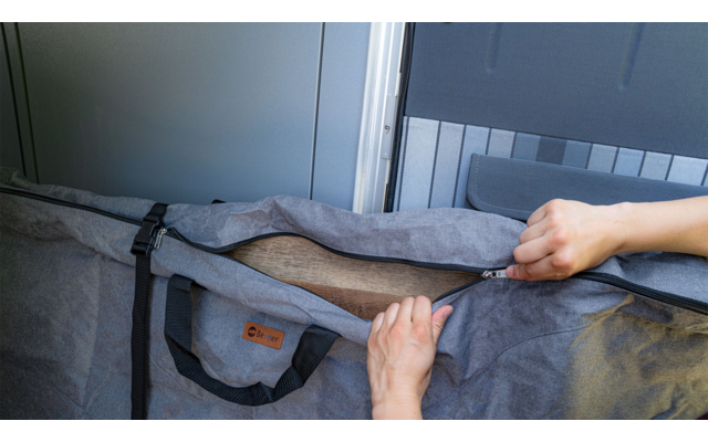 Hands opening a zipper on a gray fabric bag