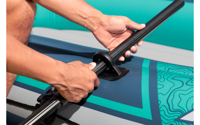 Hände stecken ein Paddel in eine Halterung auf einem türkis-blauen aufblasbaren Stand-up-Paddle-Board mit Muster