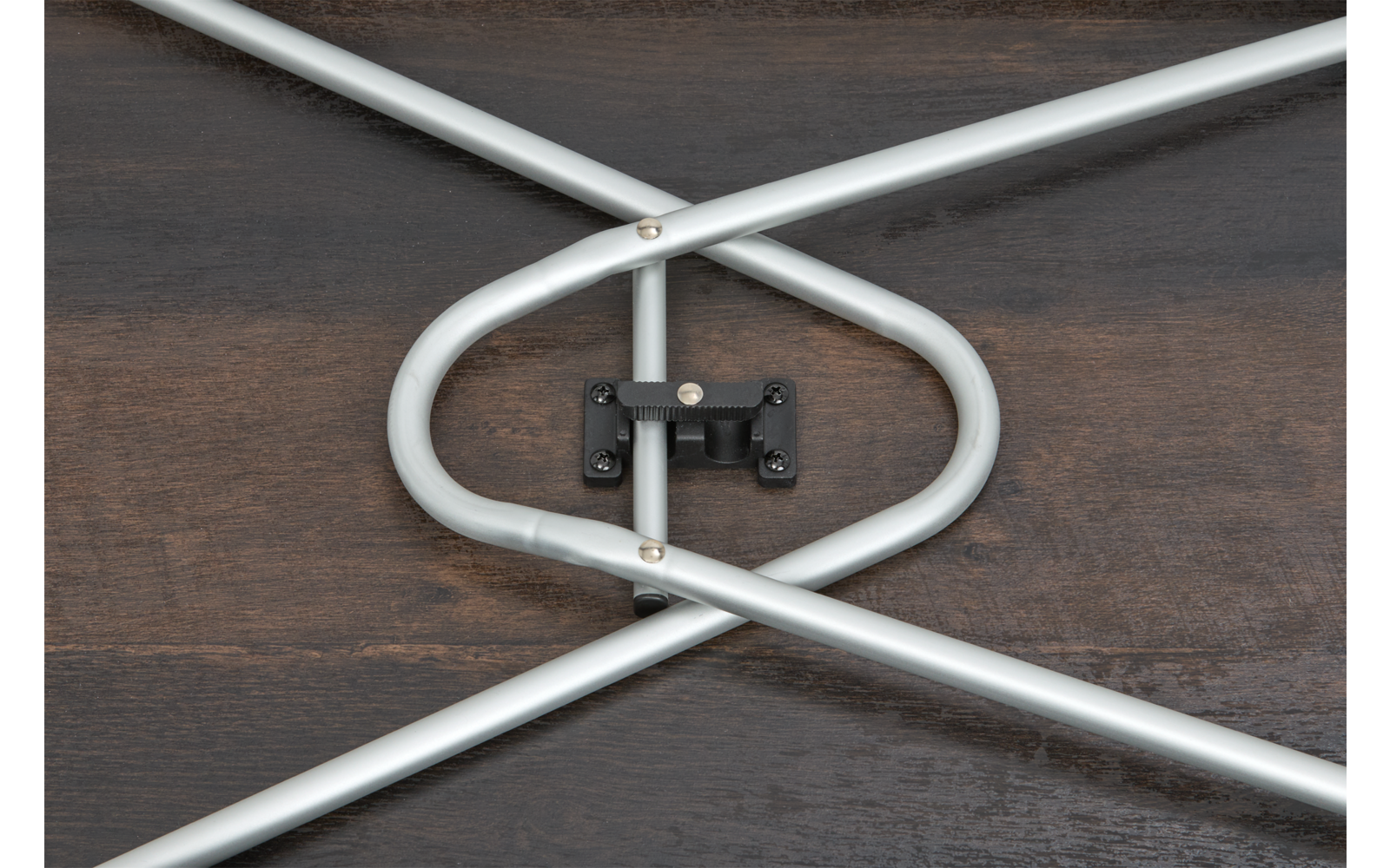Tubes métalliques argentés croisés reliés par une charnière noire sur une surface en bois foncé