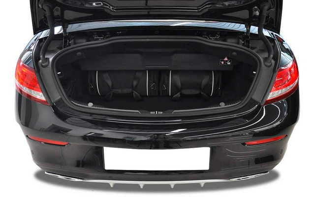 Coffre ouvert d'une voiture noire avec trois sacs de voyage noirs à l'intérieur, feux arrière visibles et plaque d'immatriculation blanche