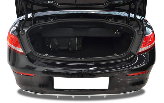 Coffre ouvert d'une voiture noire, deux petits sacs noirs à l'intérieur, feux arrière visibles et plaque d'immatriculation blanche