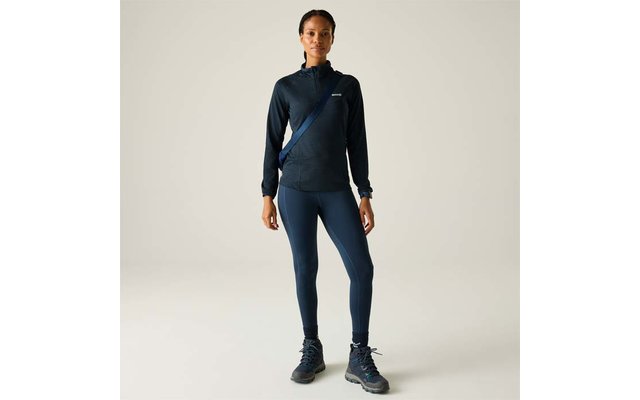 Personne debout de face sur fond clair, portant un haut de sport sombre à manches longues avec fermeture éclair, un legging sombre, une bandoulière en travers de la poitrine et des chaussures de randonnée