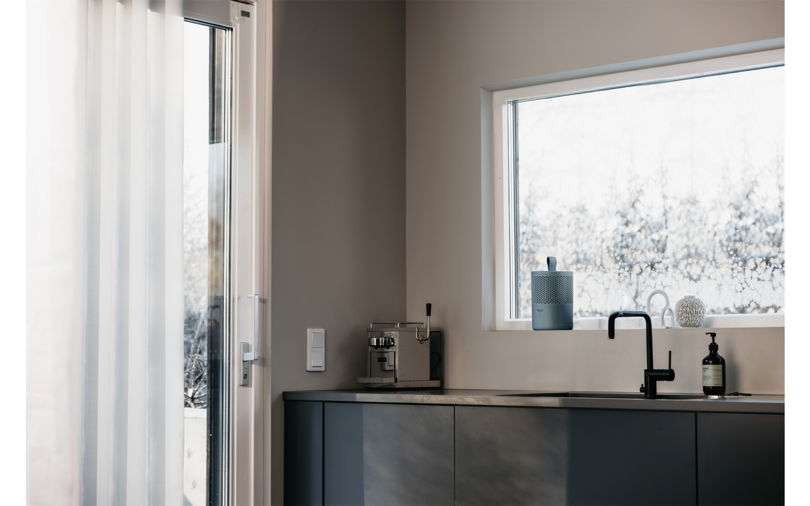 Küchenzeile mit Spüle, Wasserhahn und Blick durch ein Fenster auf verschneite Bäume