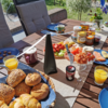 Ein gedeckter Gartentisch mit Brötchen, Gläsern mit Orangensaft, Marmeladengläsern und Schalen mit Erdbeeren