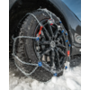 Plano detalle de un neumático de coche con cadenas para nieve en una llanta negra, nieve en el suelo y sobre las cadenas