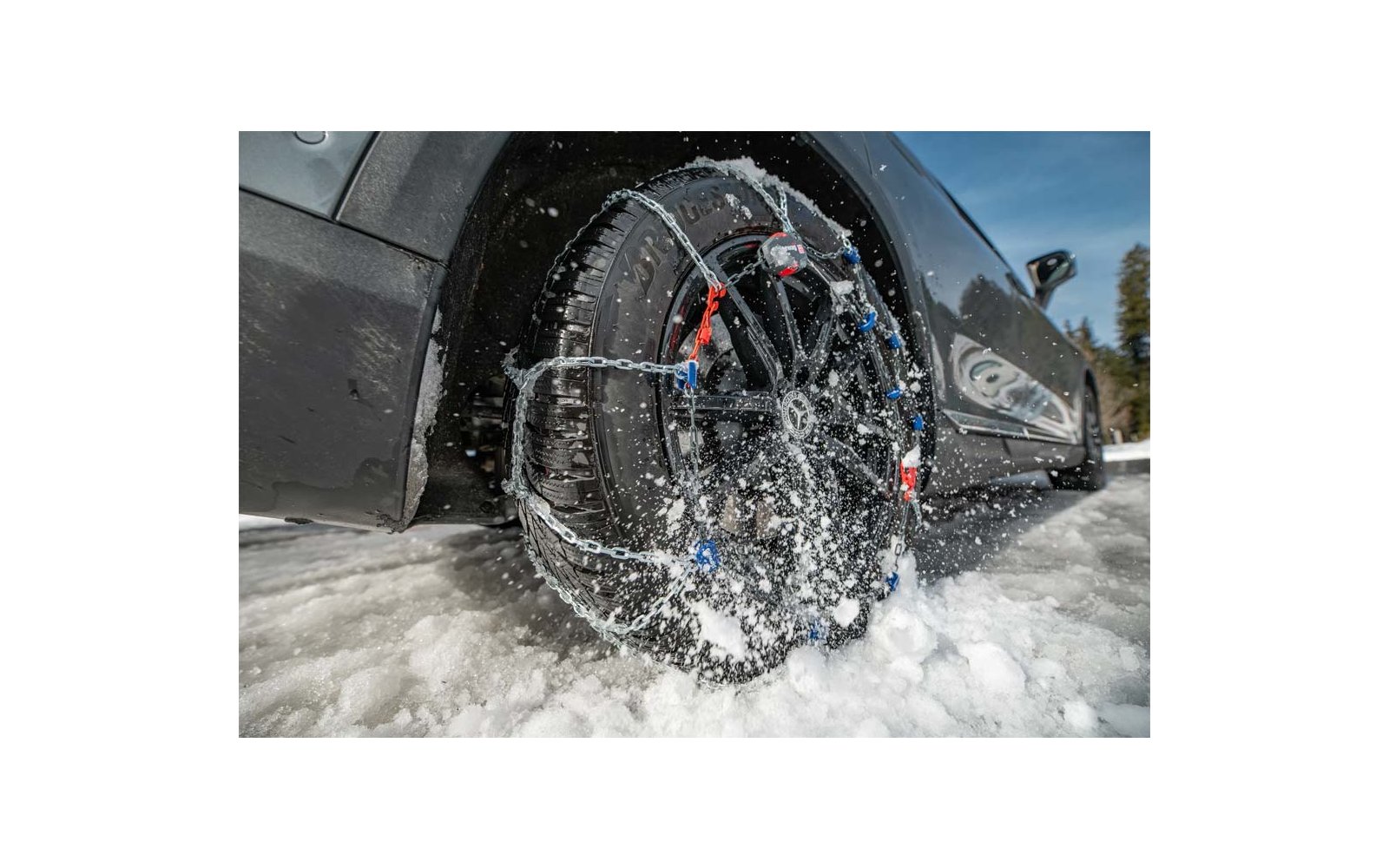Primer plano de un neumático de coche con cadenas para la nieve, salpicaduras de agua, coche negro y nieve en la carretera