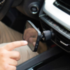 Hand berührt Smartphone, befestigt an der Lüftungsdüse eines Autos mit magnetischer Halterung; Armaturenbrett und Startknopf sichtbar