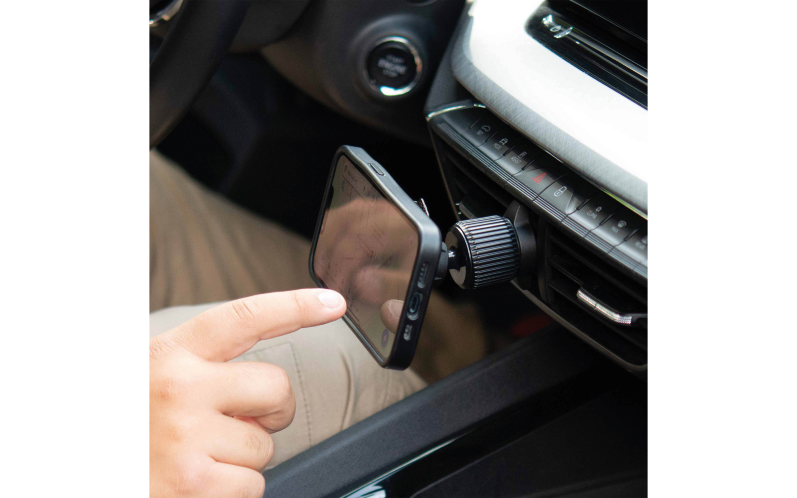 Hand berührt Smartphone, befestigt an der Lüftungsdüse eines Autos mit magnetischer Halterung; Armaturenbrett und Startknopf sichtbar