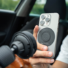 Hand hält ein silbernes Smartphone mit rundem schwarzem Pad auf der Rückseite, Autoinnenraum im Hintergrund