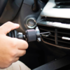 Hand setzt schwarzen Halter in die Lüftungsdüse eines Autos; Armaturenbrett und Zündschloss sichtbar