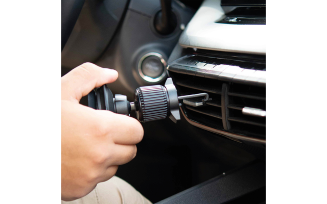Hand setzt schwarzen Halter in die Lüftungsdüse eines Autos; Armaturenbrett und Zündschloss sichtbar