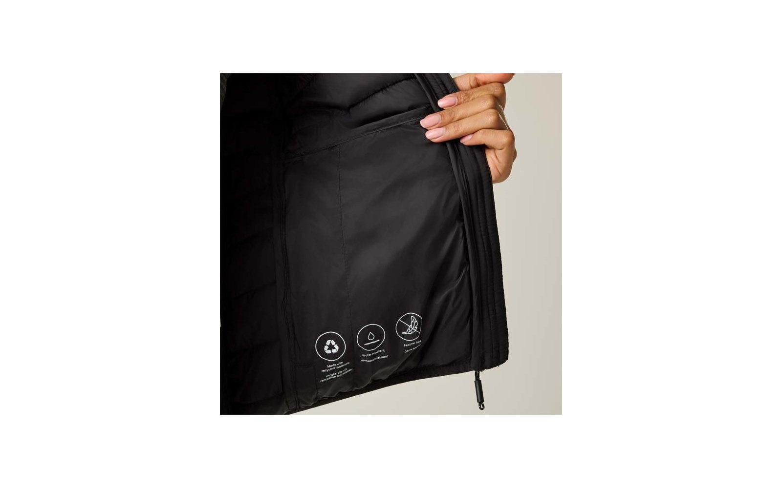 Hand hält eine geöffnete schwarze Jacke, Innenfutter sichtbar mit drei weißen Kreis-Symbolen und kleinem Text, Reißverschluss-Zipper und beiger Hintergrund