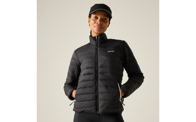 Person in schwarzer gesteppter Jacke und schwarzer Kappe, Hände in den Taschen, heller einfarbiger Hintergrund