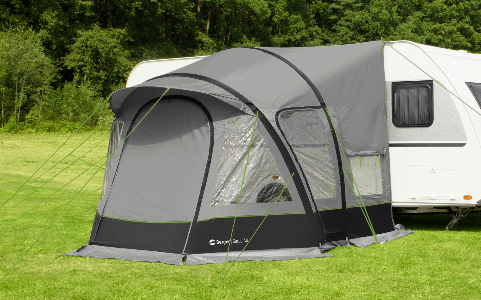 Weißer Wohnwagen mit grauem Vorzelt auf grüner Wiese vor Bäumen und blauem Himmel